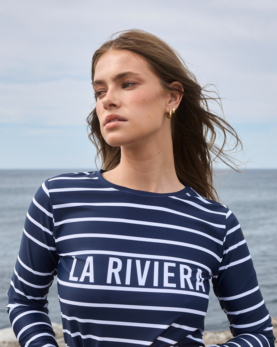 Model in ACQUA Brand La Riviera navy striped long sleeve rashguard with UPF50+ sun protection by the sea