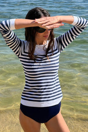 Woman wearing the ACQUA classic long sleeve UPF50+ rashguard in navy stripe, standing in the ocean.