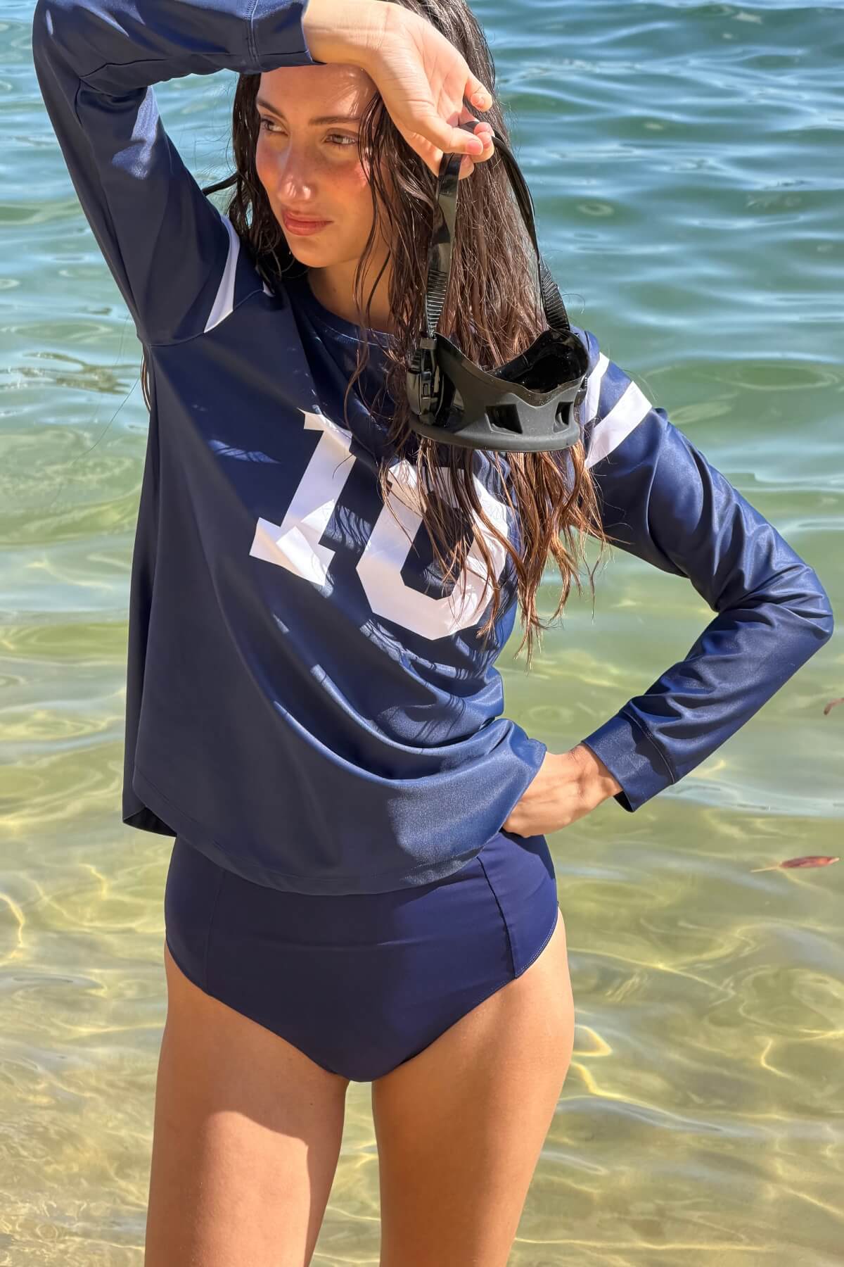 Woman wearing the ACQUA Perfect 10 UPF50+ rash guard in navy and white, standing in the ocean.