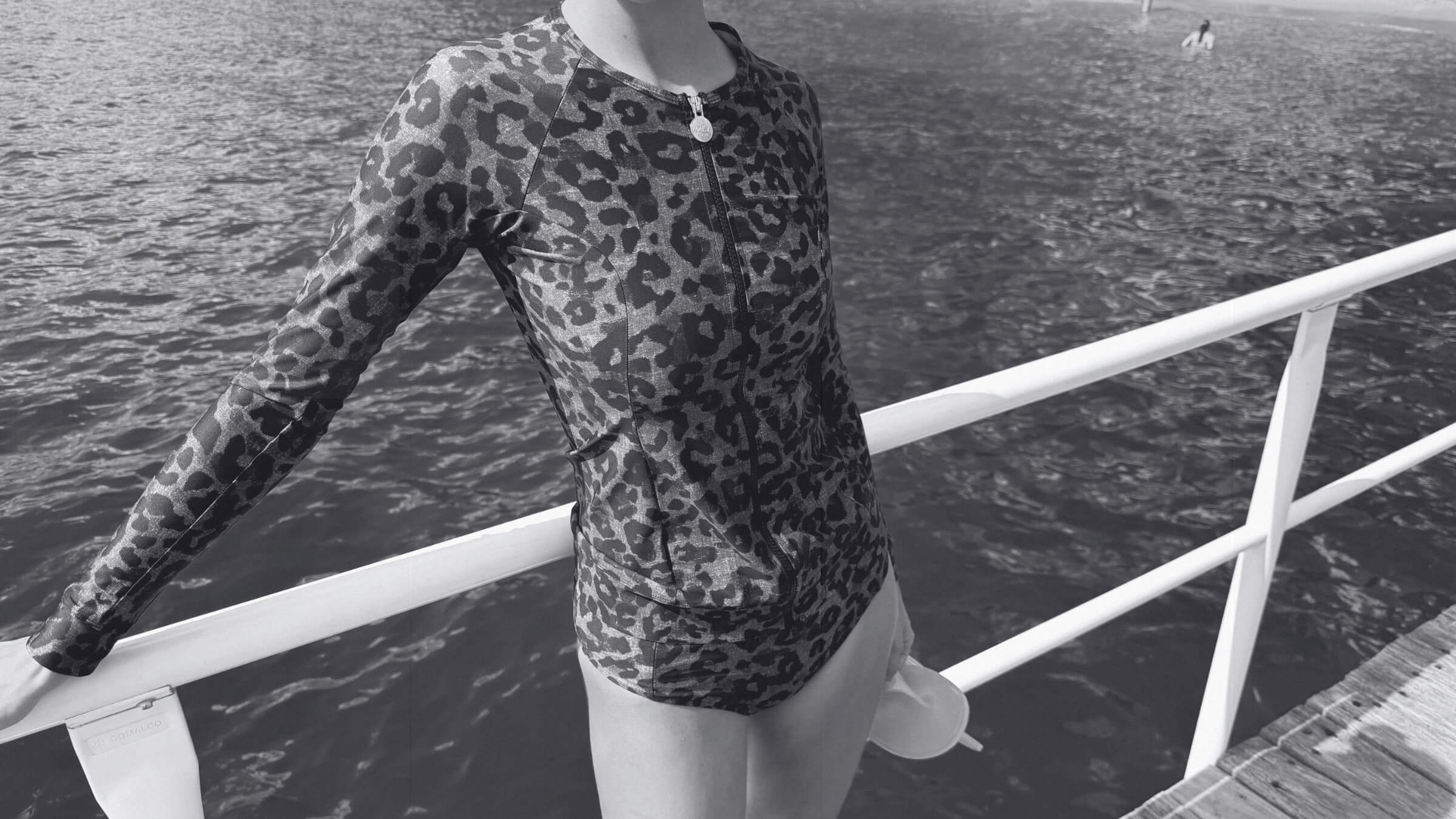 Woman wearing the ACQUA leopard print zip long sleeve UPF50+ rashie with gold zipper, standing by the water.