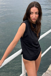 Woman wearing the ACQUA relaxed swim tank in black with UPF50+ sun protection, standing by the water.